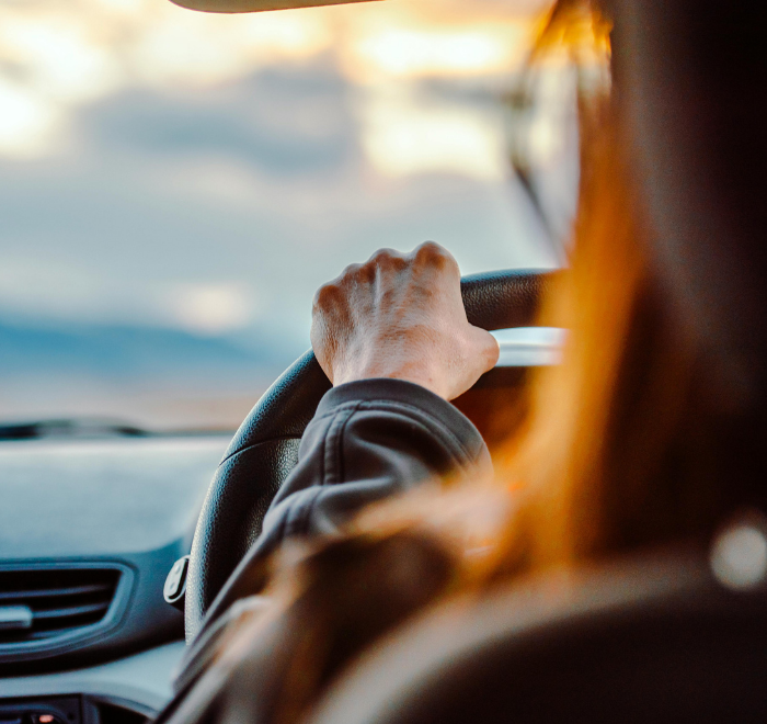 Woman with long red hair driving a car in the low sunshine with her hands on the steering wheel